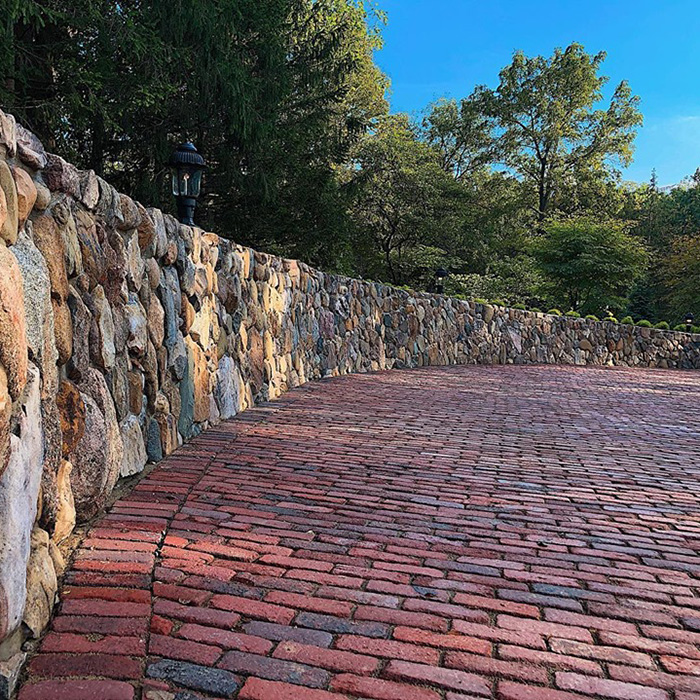Entrance parking pad of reclaimed bricks next to an antique stone wall