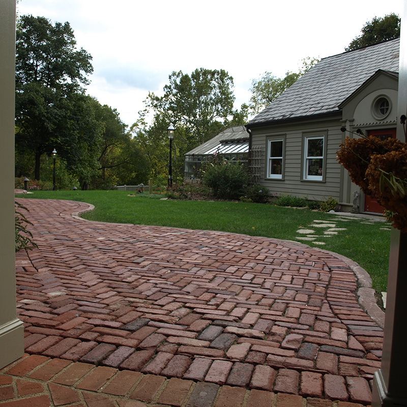 Curved sidewalk of salvaged street brick pavers installed in herringbone pattern