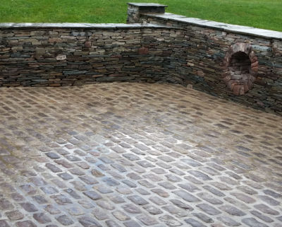 The landscaping of this backyard is enhanced by an antique cobblestone patio
